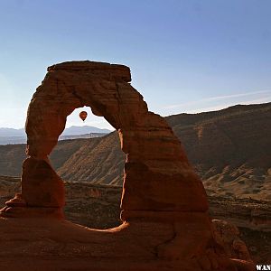 Delicate Arch with hot air balloon drifting by, seen through arch.