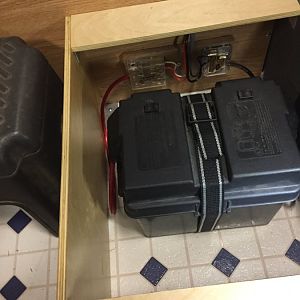 battery box strapped to floor with vent grate over turnbuckle access hole