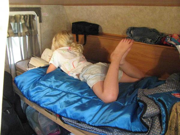 My daughter enjoying a book in the lower bunk area of our trailer.