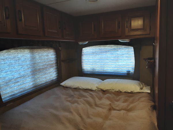 Queen bed with cabinets along side and back wall